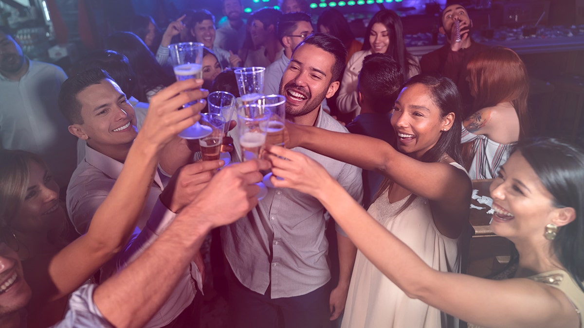 Group of friends toasting glasses at nightclub during busy celebration.