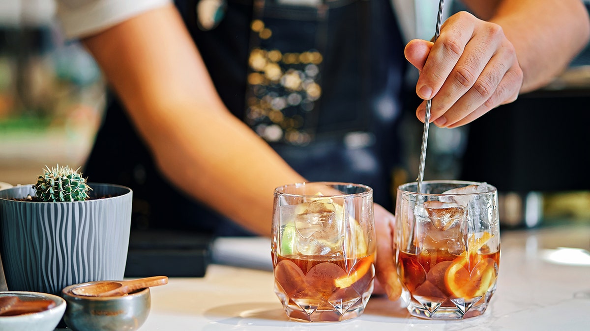 Bartender stirring two cocktails with ice and citrus slices on a bar counter.