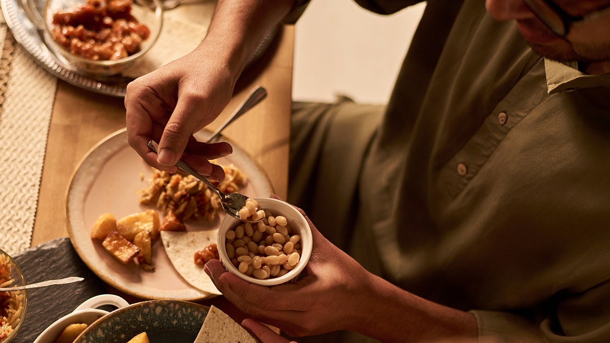 Man seen taking spoonful of beans that he's eating alongside Spanish food.