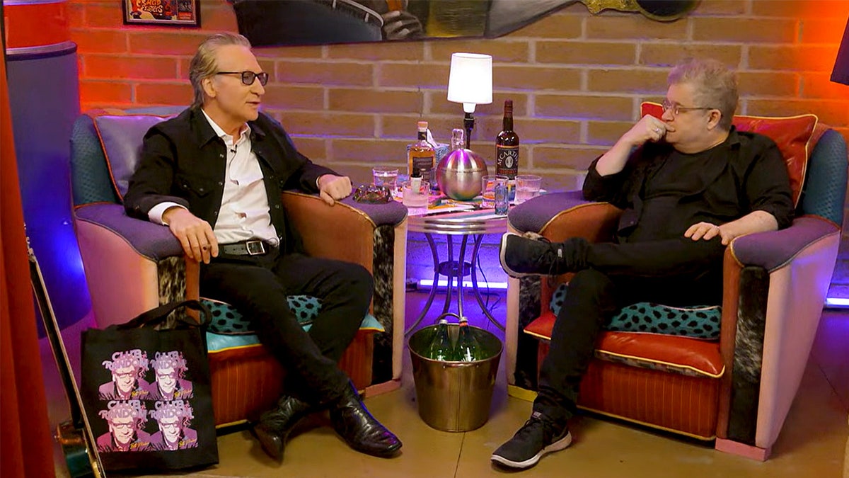 Bill Maher and Patton Oswalt are seated in an intimate, low-lit setting for his "Club Random" podcast.