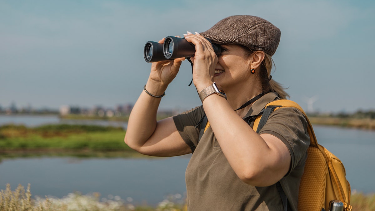Woman using binoculars for birdwatching in the outdoors.