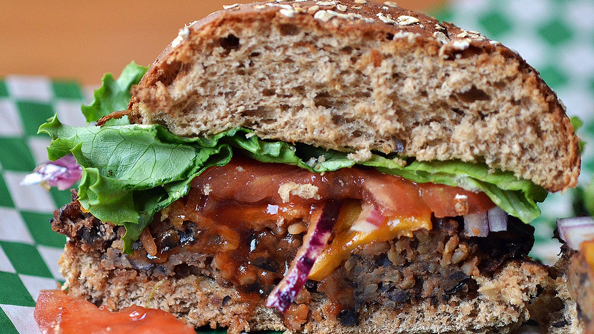 Black bean burger on checkered paper, served on whole grain bun with lettuce, tomato and onion.
