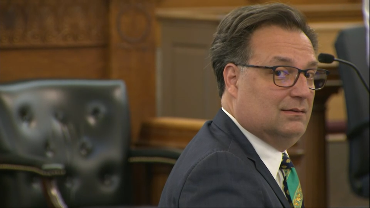 Brian Walshe looking over his shoulder in court. He is clean-shaven, wearing glasses and a dark suit with green tie.