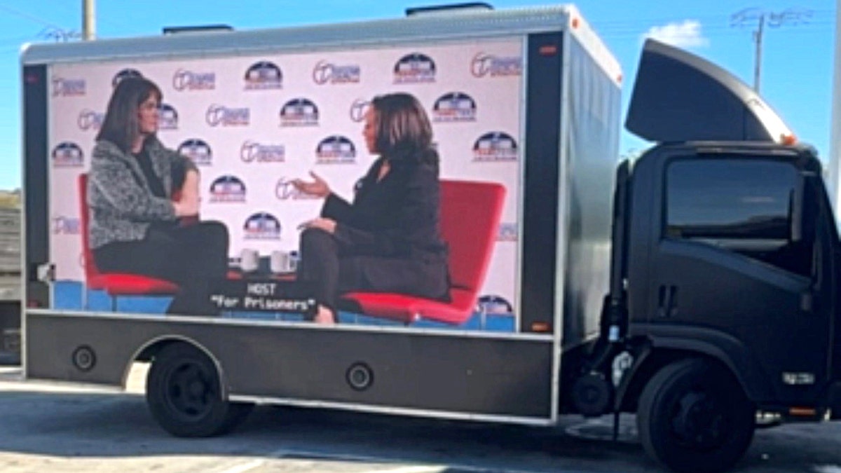 Kamala Harris and another individual displayed on a screen on the side of a truck
