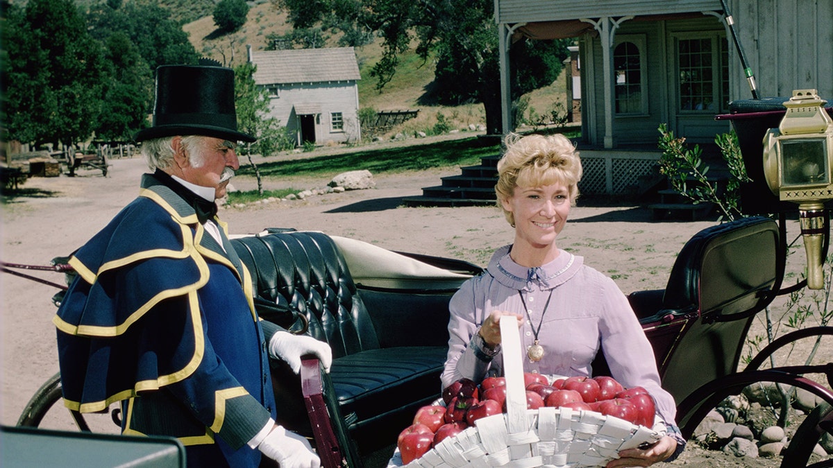 Charlotte Stewart as Miss Beadle holding a basket of apples.