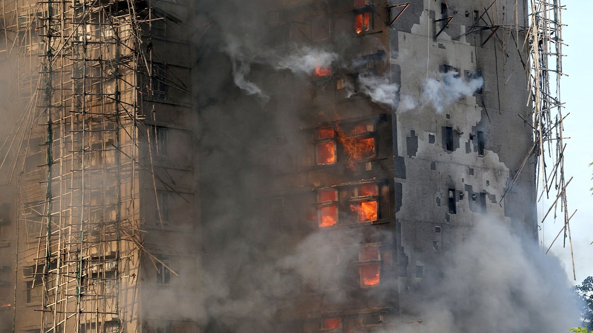 Fire sweeps through bamboo scaffolding as thick smoke rises above a residential complex.
