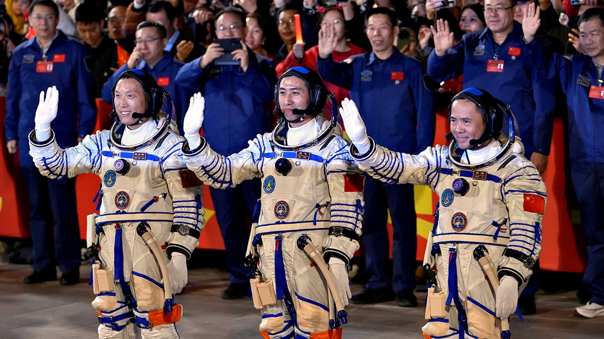 Los astronautas chinos se paran y saludan con trajes espaciales para la misión Shenzhou-21