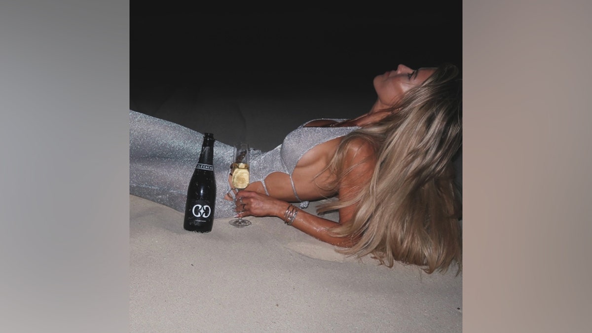 Christina Haack lounges on the sand in a sparkly silver dress while promoting her new Clé Cachée champagne line.