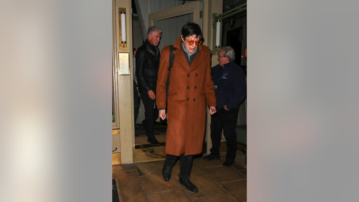 Christopher Brosnan leaves Dorian restaurant in London after a family dinner, wearing an orange overcoat and glasses, followed by his father Pierce Brosnan.