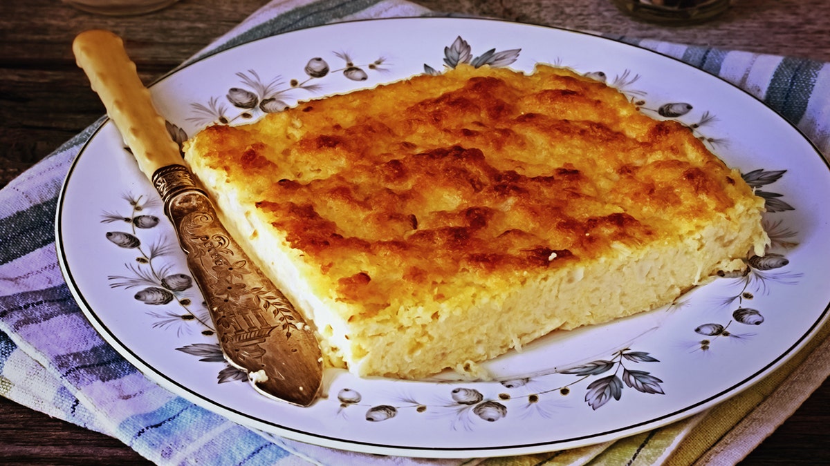 Vintage corn pudding seen on porcelain plate with gold knife.