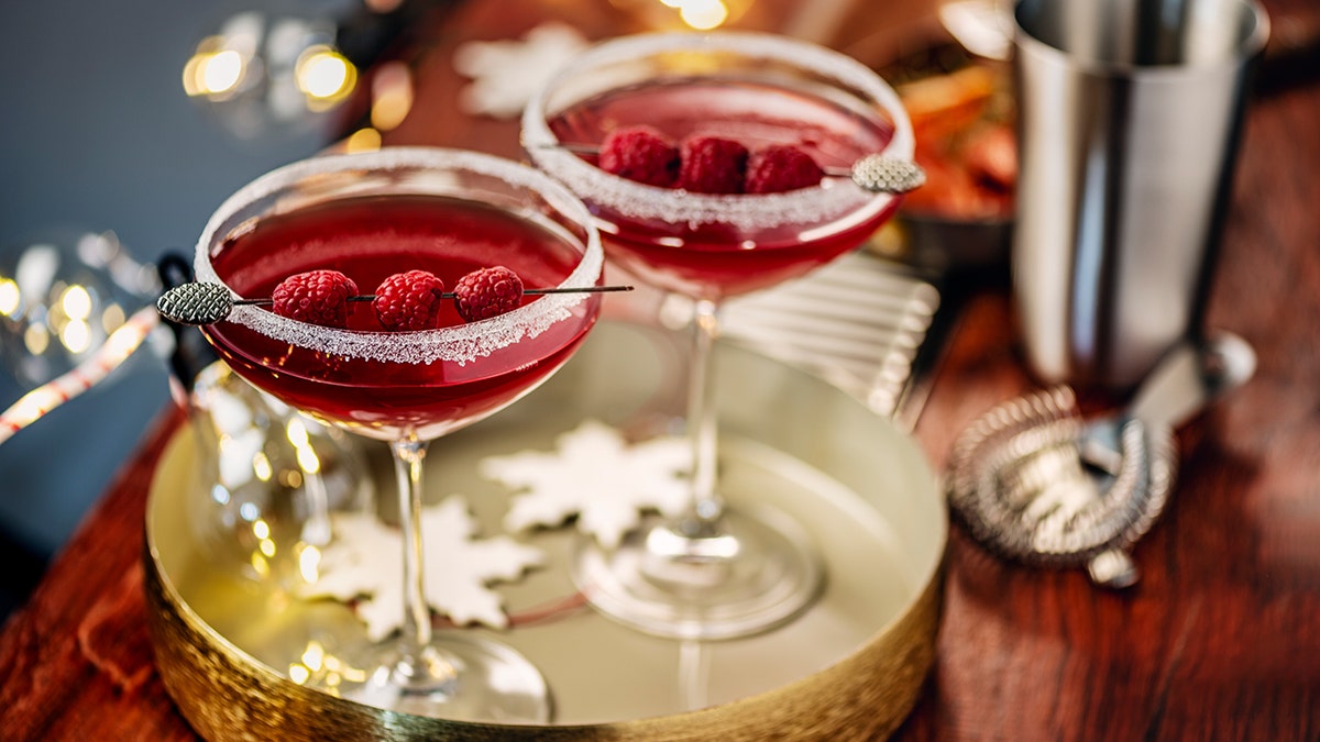 Two red raspberry cocktails in sugar-rimmed glasses on a festive tray.