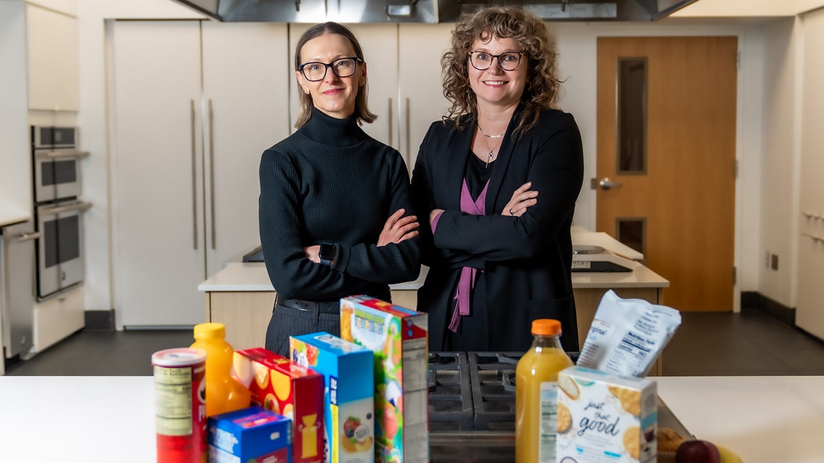 Virginia Tech scientists Brenda Davy, left, and Alex DiFeliceantonio smile and pose with junk food and a variety of healthy foods in front of them.