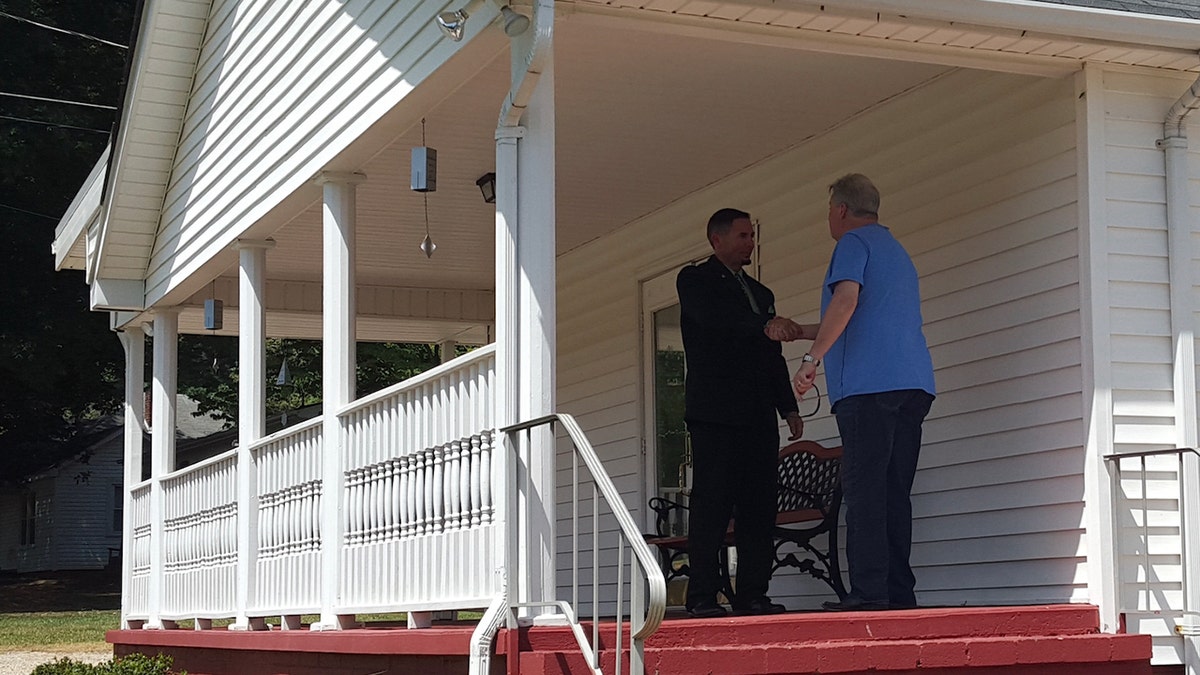 A priest and a person shaking hands outside the church porch.