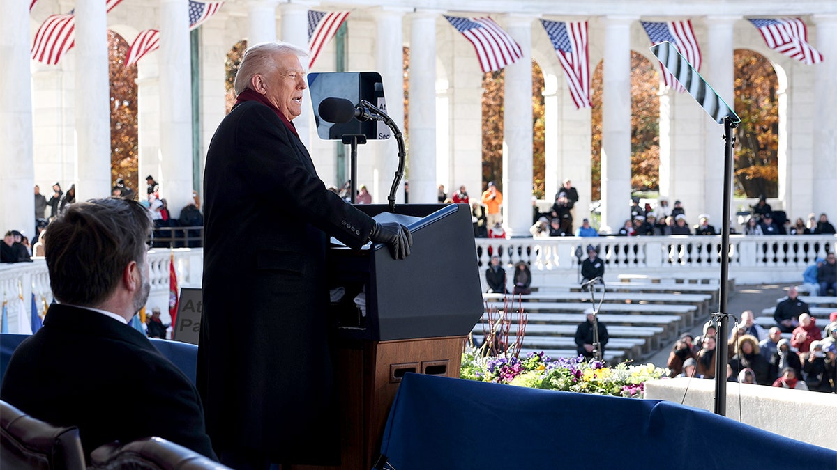 President Donald Trump speaks at a Veterans Day ceremony at Arlington National Cemetery with Vice President JD Vance seated beside him.