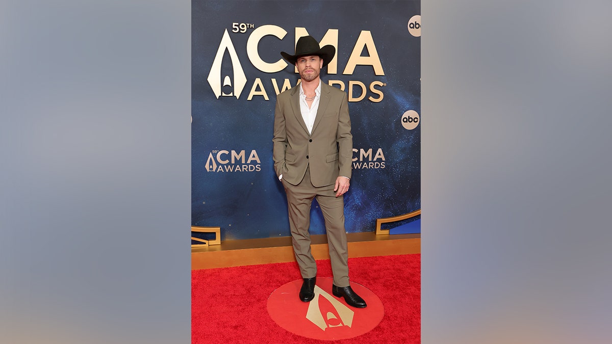 Dustin Lynch at the CMA Awards 2025 in a tan suit and cowboy hat.