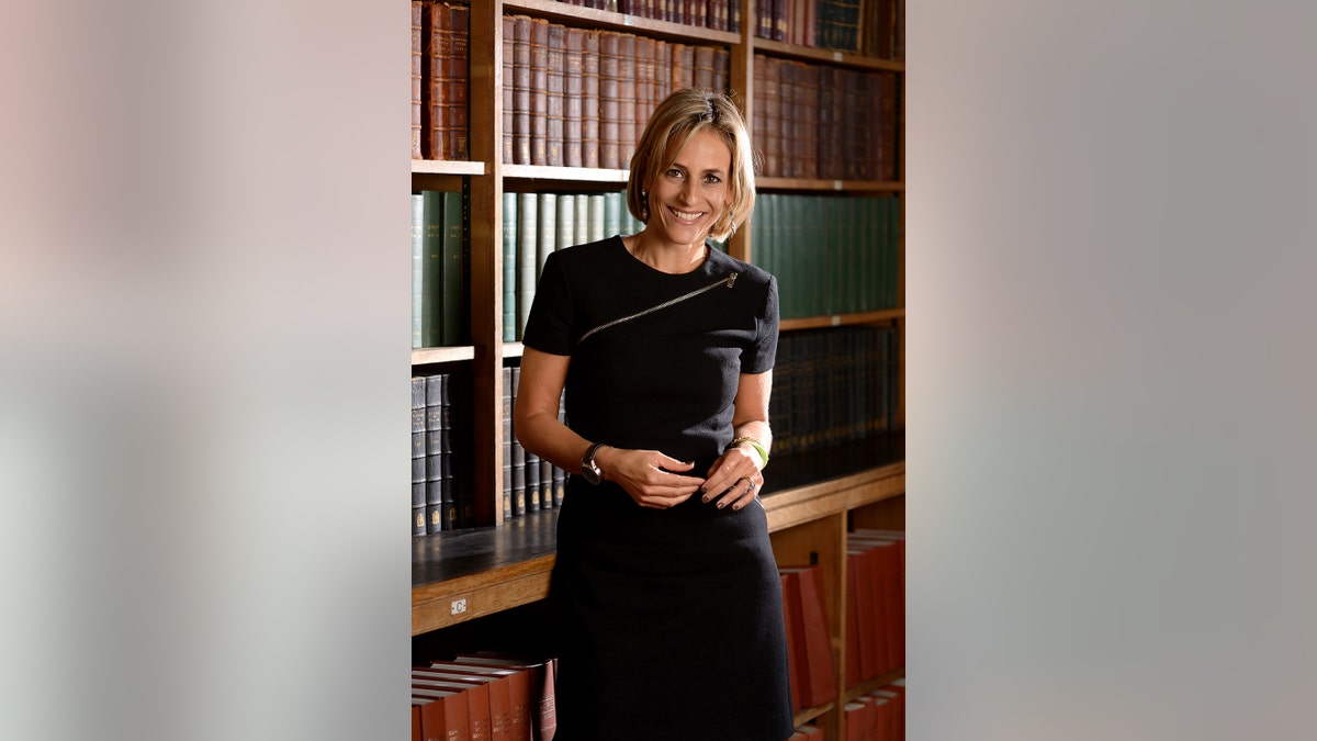 Emily Maitlis wearing a black dress smiling in front of a library.