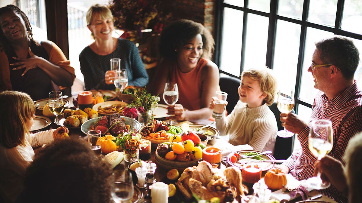 A joyful group of people gathered around a festive dinner table, raising glasses and sharing a meal together.