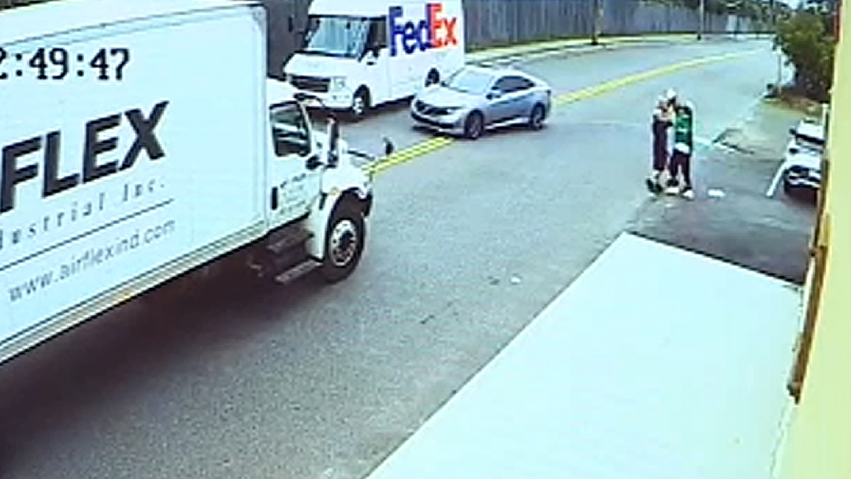 A still image from video shows two alleged thieves grabbing a package from a FedEx driver with the getaway vehicle waiting steps away
