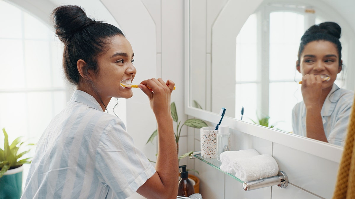 Female brushing her teeth in front of a bathroom mirror.