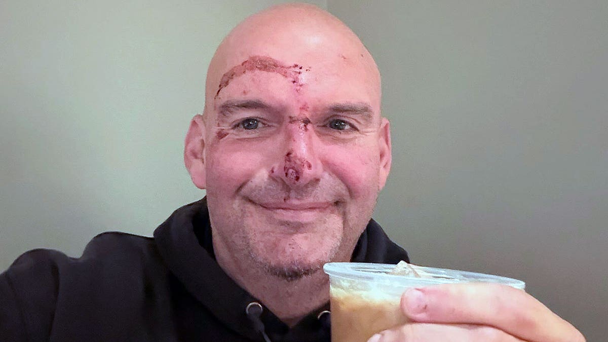 Senator Fetterman with stitches holding iced coffee in selfie