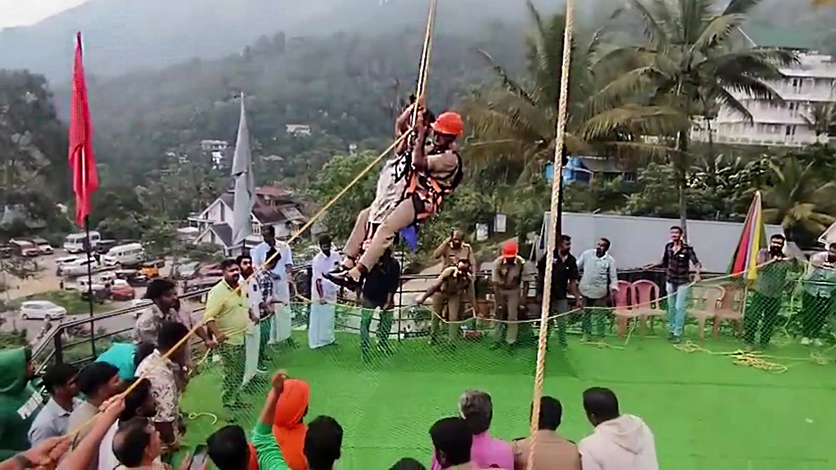 Firefighter rescues family by climbing a rope, while a crowd watches.