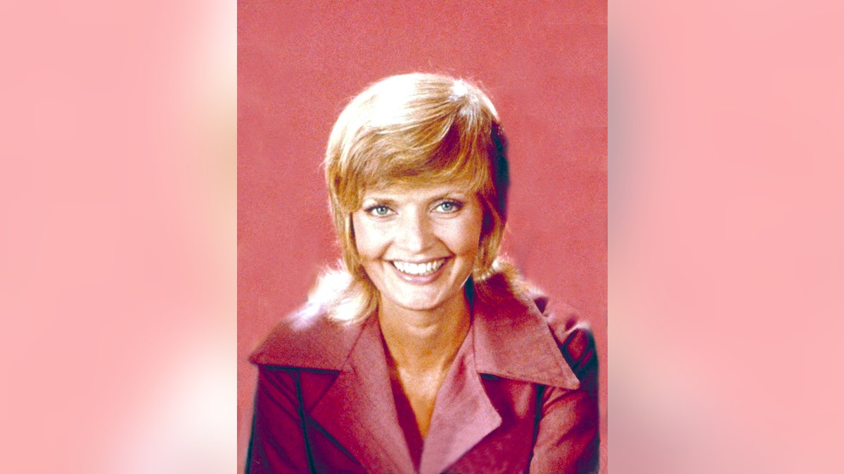 弗洛倫斯·亨德森 (Florence Henderson) 飾演卡羅爾·布雷迪 (Carol Brady),身穿珊瑚色襯衫微笑。