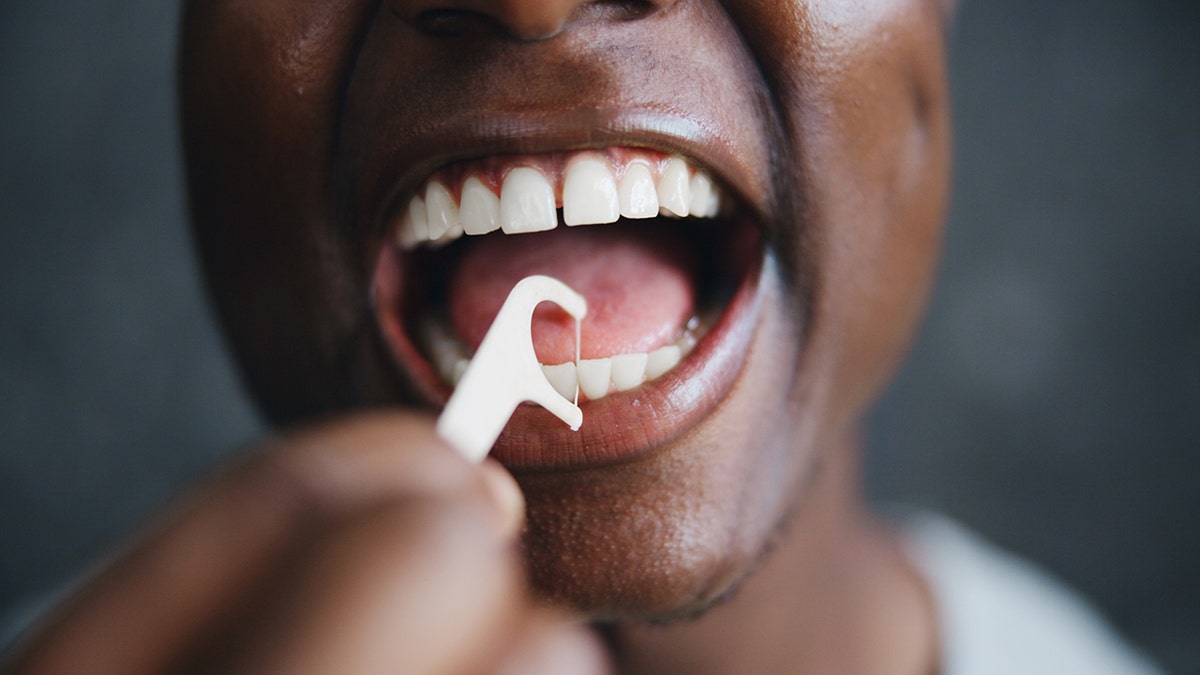 Close-up of person using floss pick on bottom teeth.