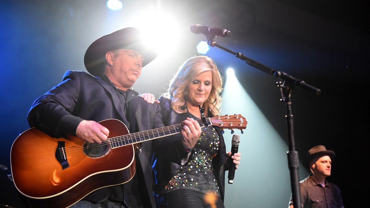 Garth Brooks plays the guitar while Trisha Yearwood holds a microphone