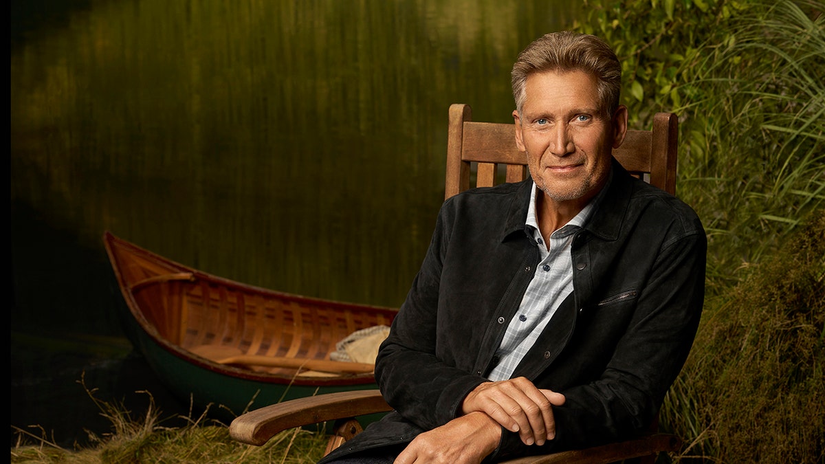 Gerry Turner wearing a dark blazer sitting on a wooden chair outdoors.