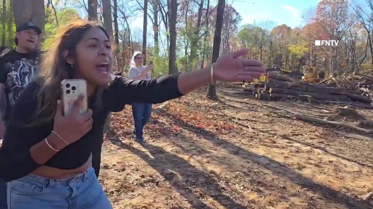 A woman holding a phone yells toward federal agents in a wooded area during a protest in Charlotte, North Carolina, as part of a confrontation with Border Patrol and Homeland Security officers on Nov. 16, 2025.