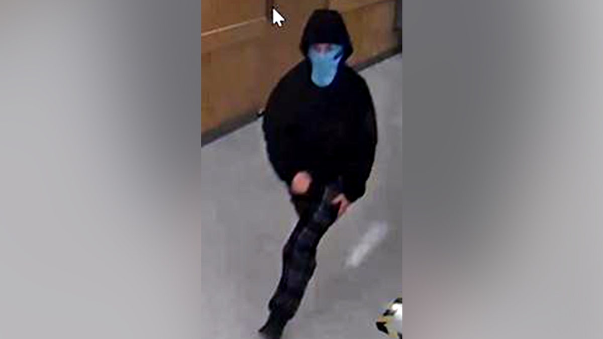 A surveillance image of one suspect in a light blue face covering and black hoodie