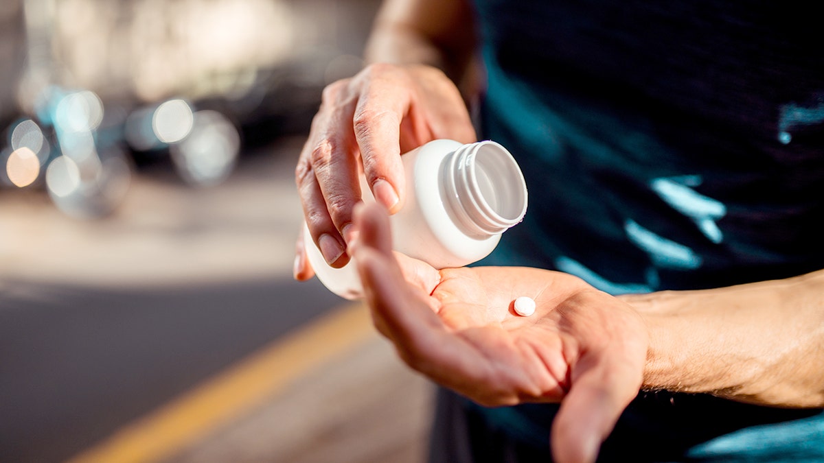 Man holding the medicine bottle in one hand and pill in other