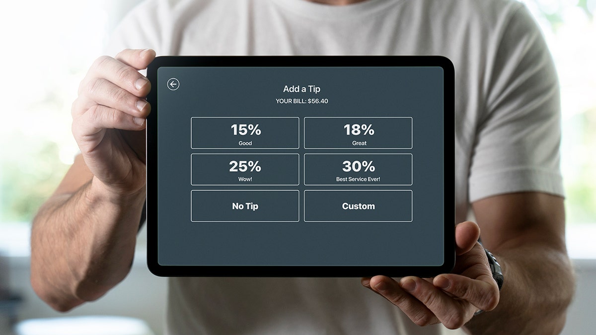 A man in a white shirt holds a tablet with percentage-based tips on the screen.