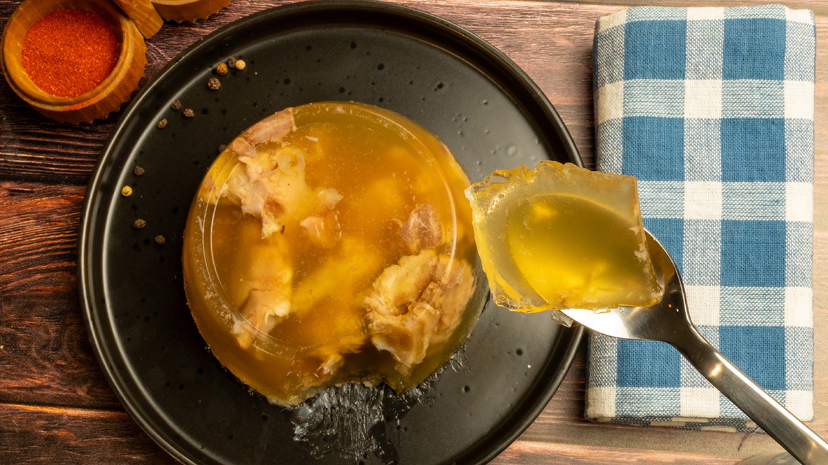Spoon scooping savory jelly from aspic mold with meat or fish in it.
