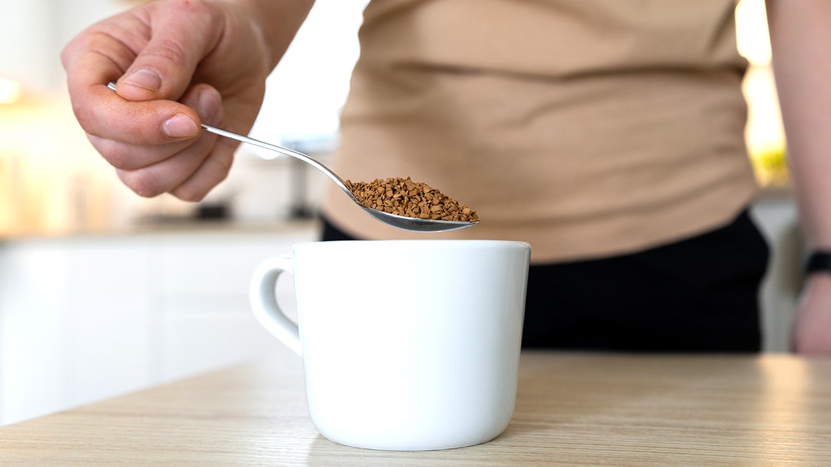 Spoon holding instant coffee being placed into mug