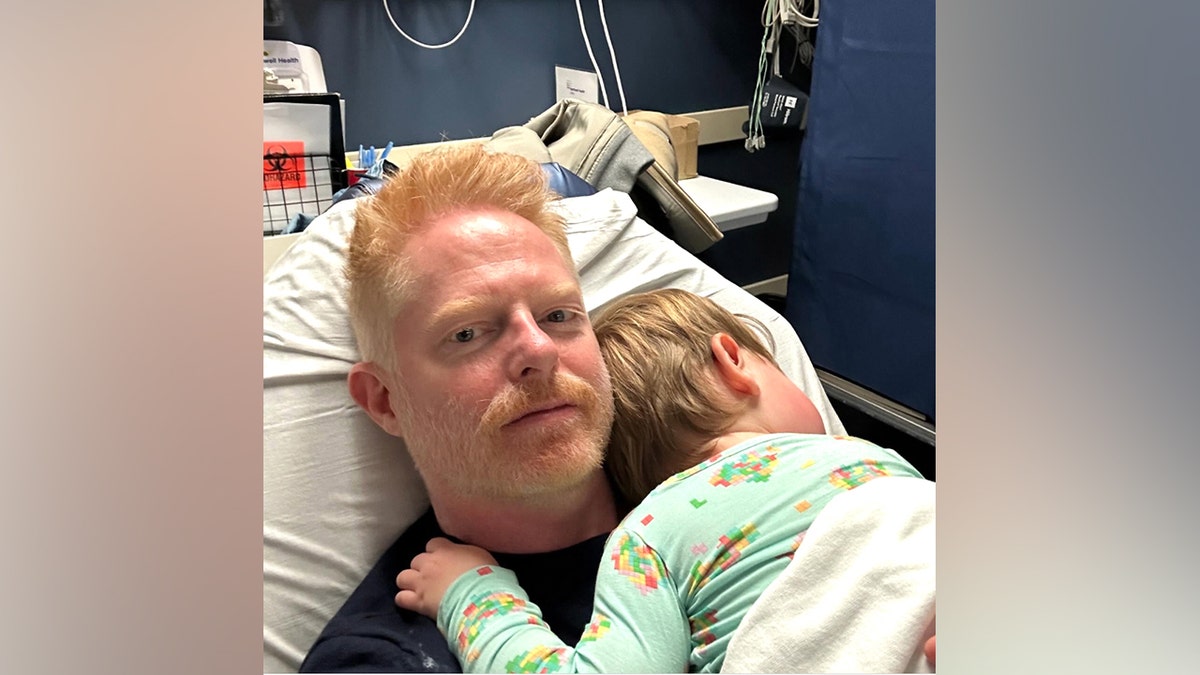 Jesse Tyler Ferguson lies in a hospital bed holding a child during a Thanksgiving 2024 ER visit, in a photo he shared on Instagram.
