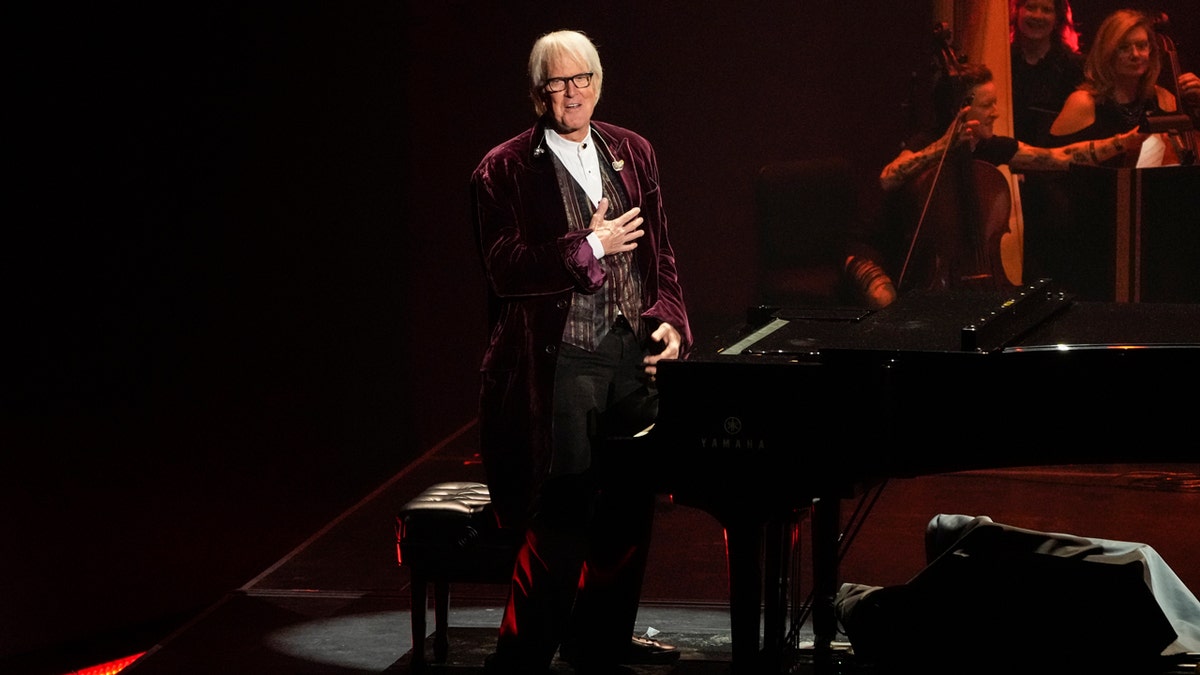 John Tesh stands by the piano
