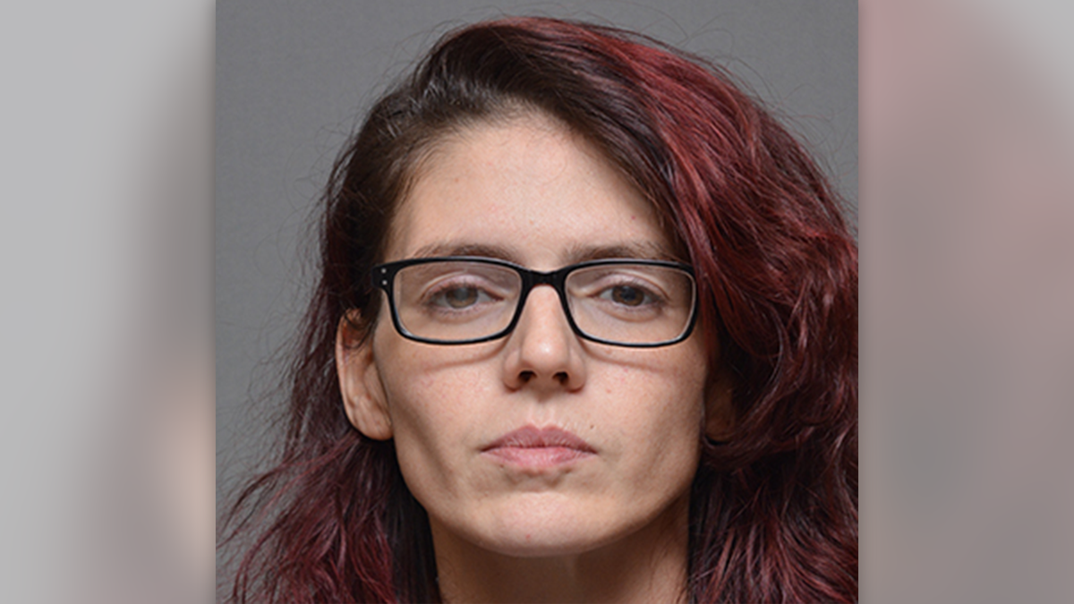 Kacy Corso wearing black glasses with red dye in her hair in a mugshot