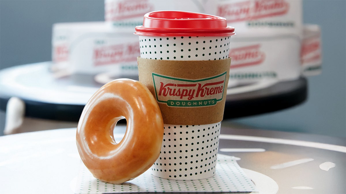 A Krispy Kreme glaze doughnut rests on a coffee cup.