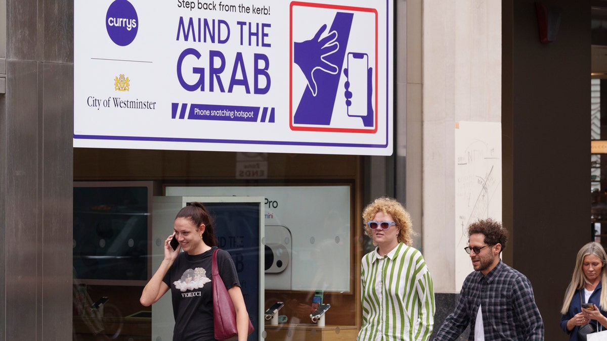 Girl on phone and other pedestrians on oxford street in front of mind the grab sign