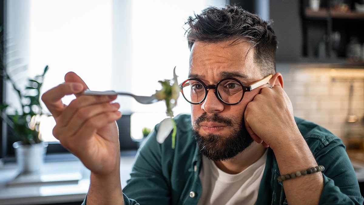 A sad man looks at a green salad fork