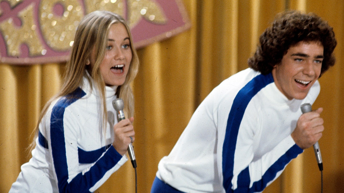 莫琳·麥考密克和巴里·威廉姆斯穿著相配的服裝在舞台上唱歌。