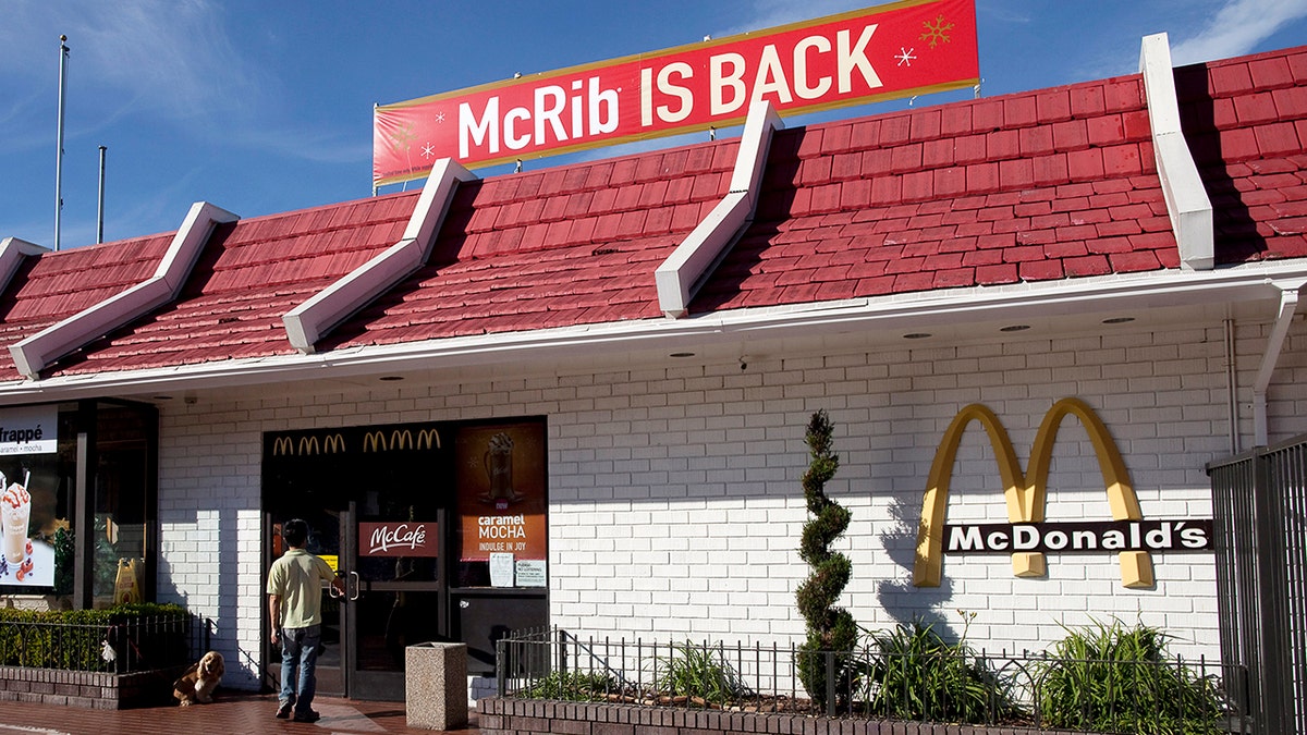 Person walking into mcDonald's with dog and "McRib is back" sign on top of building.