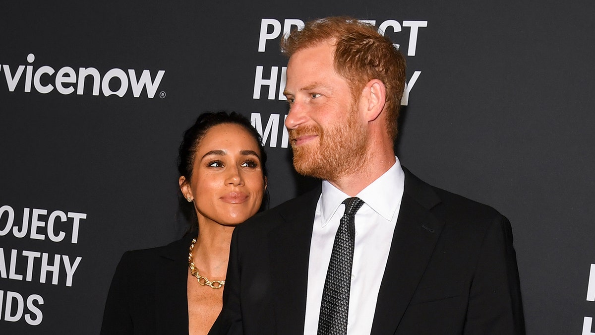Meghan Markle admiring Prince Harry as they both wearing matching black outfits.