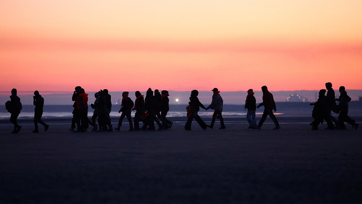Migrants walk along the beach before trying to board an inflatable dinghy