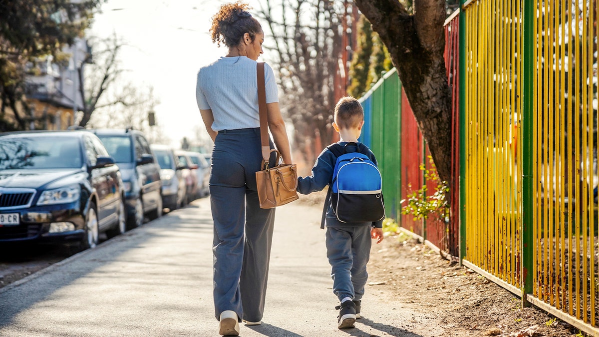 Mother and son hold hands while walking on a sidewalk