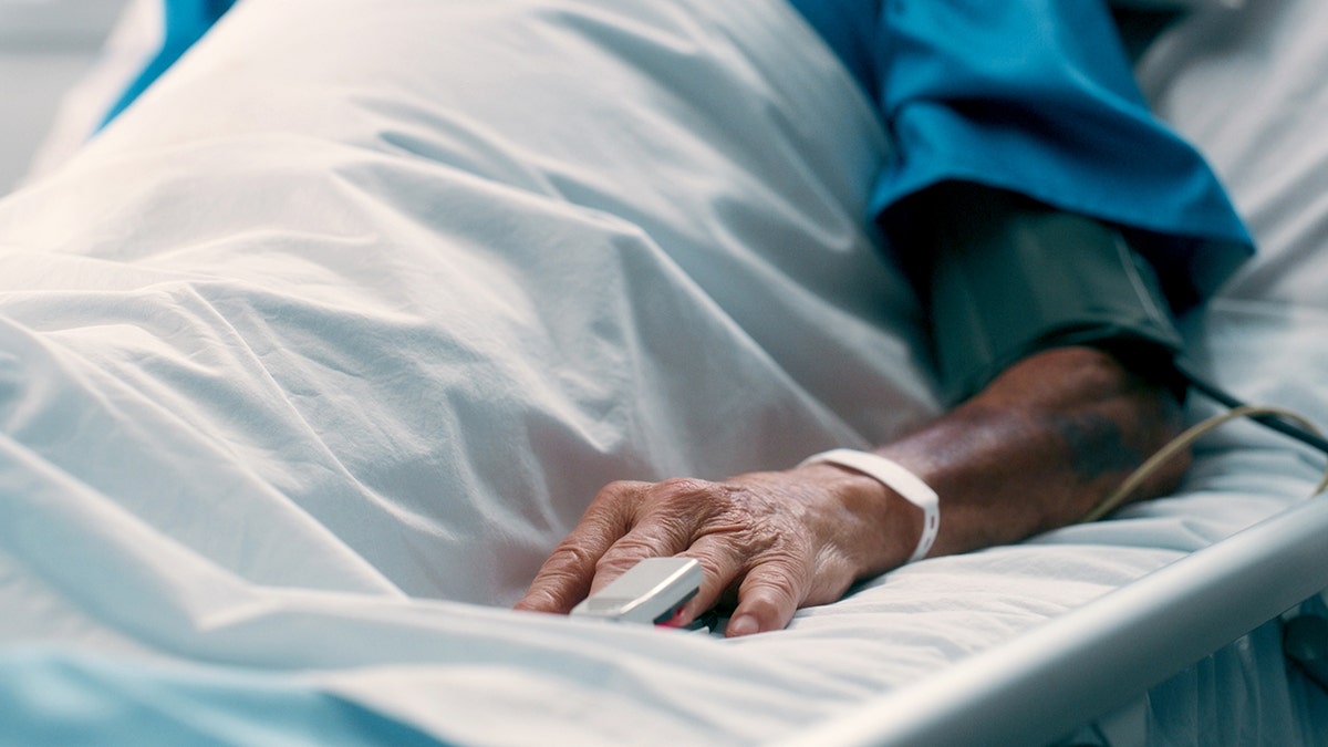 Older man in hospital bed, only hand is shown