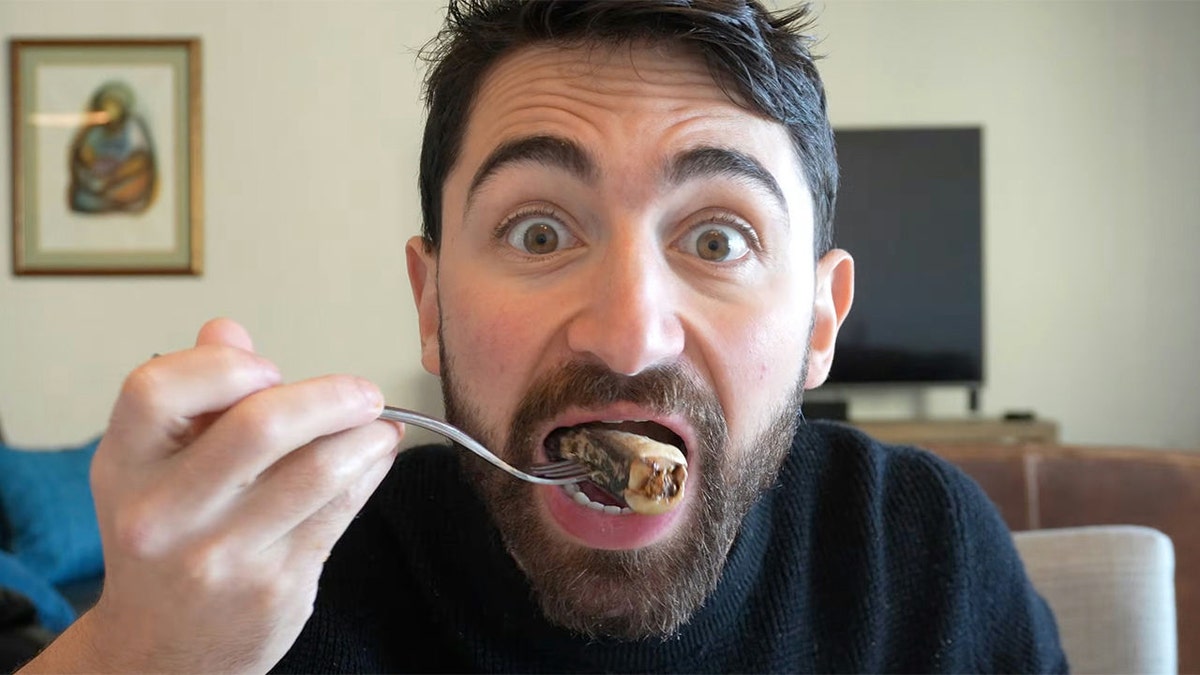 Dr. Nick Norwitz eating sardine on fork, seen biting in with eyes wide open in living room.