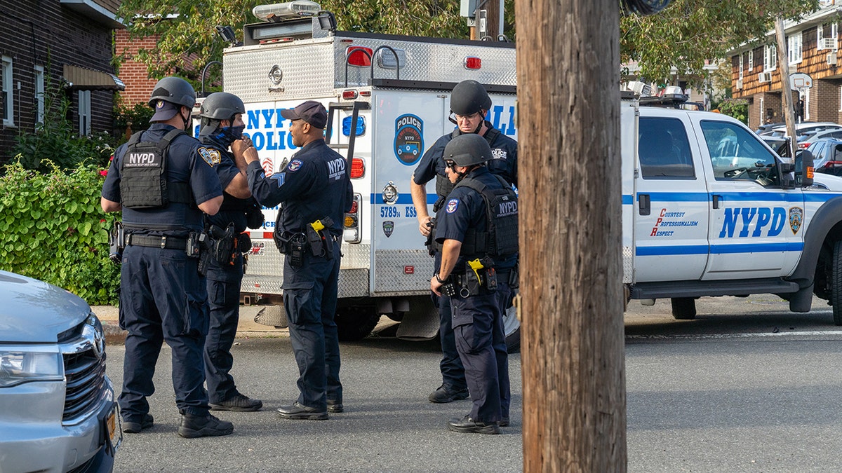 NYPD officers in helmets and bulletproof vests standing near police vehicle on street