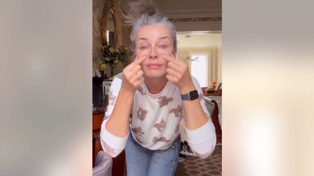 Paulina Porizkova pinching her cheeks